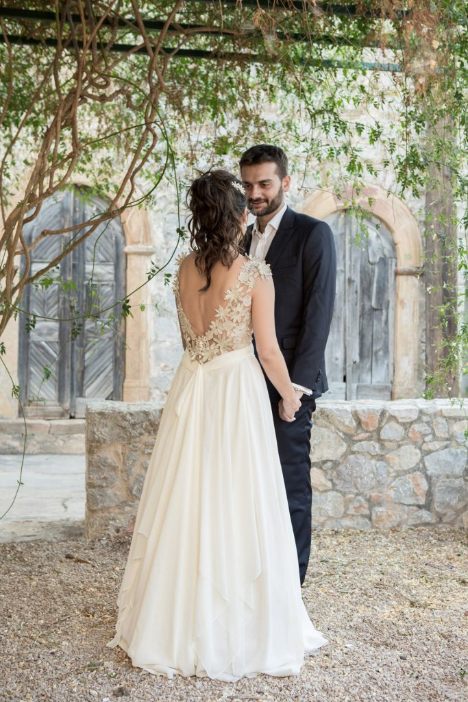 Romantic bride and groom portrait framed by soft greenery, captured against a rustic stone wall in a sun-washed Mediterranean setting. Their warm smiles and tender gaze create an intimate, timeless moment—perfect for destination wedding photography in a charming historic village.