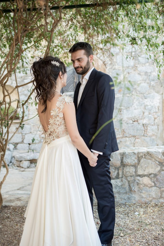 Romantic bride and groom portrait framed by soft greenery, captured against a rustic stone wall in a sun-washed Mediterranean setting. Their warm smiles and tender gaze create an intimate, timeless moment—perfect for destination wedding photography in a charming historic village.