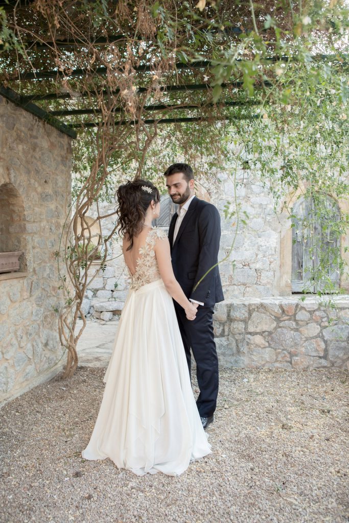 Romantic bride and groom portrait framed by soft greenery, captured against a rustic stone wall in a sun-washed Mediterranean setting. Their warm smiles and tender gaze create an intimate, timeless moment—perfect for destination wedding photography in a charming historic village.