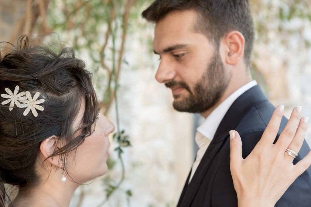 Romantic bride and groom portrait framed by soft greenery, captured against a rustic stone wall in a sun-washed Mediterranean setting. Their warm smiles and tender gaze create an intimate, timeless moment—perfect for destination wedding photography in a charming historic village.