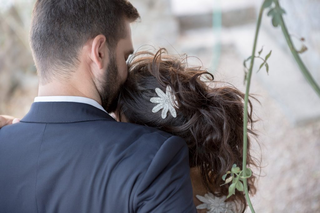 Romantic bride and groom portrait framed by soft greenery, captured against a rustic stone wall in a sun-washed Mediterranean setting. Their warm smiles and tender gaze create an intimate, timeless moment—perfect for destination wedding photography in a charming historic village.