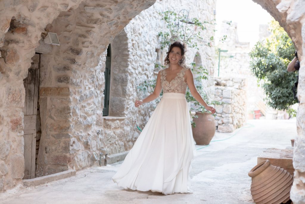 Romantic bride portrait framed by soft greenery, captured against a rustic stone wall in a sun-washed Mediterranean setting. Their warm smiles and tender gaze create an intimate, timeless moment—perfect for destination wedding photography in a charming historic village.