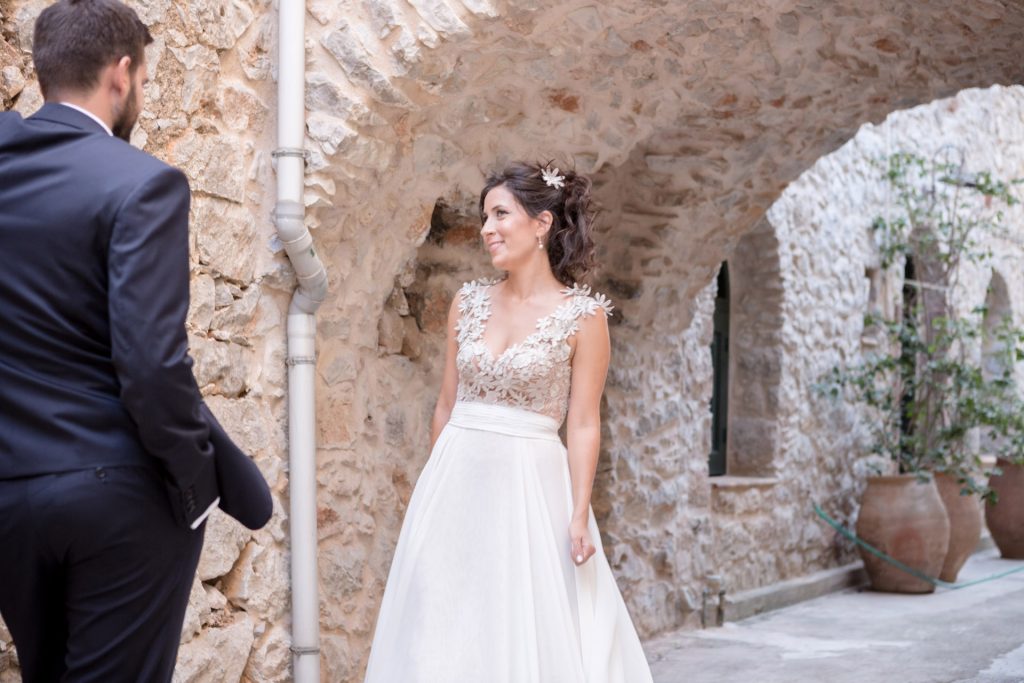 Romantic bride and groom portrait framed by soft greenery, captured against a rustic stone wall in a sun-washed Mediterranean setting. Their warm smiles and tender gaze create an intimate, timeless moment—perfect for destination wedding photography in a charming historic village.