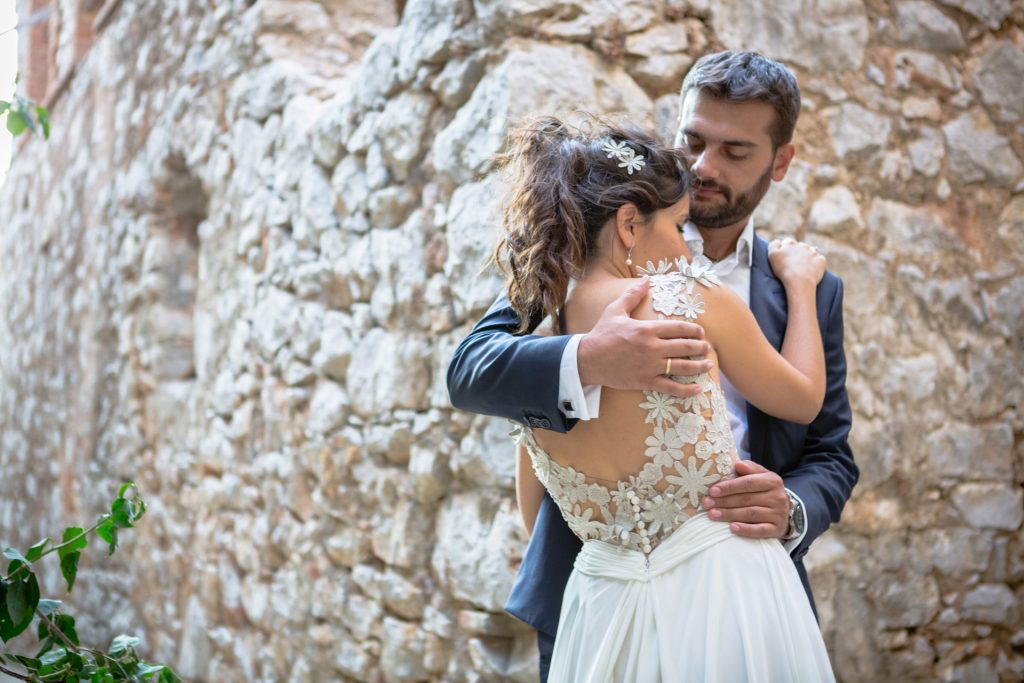 Romantic bride and groom portrait framed by soft greenery, captured against a rustic stone wall in a sun-washed Mediterranean setting. Their warm smiles and tender gaze create an intimate, timeless moment—perfect for destination wedding photography in a charming historic village.
