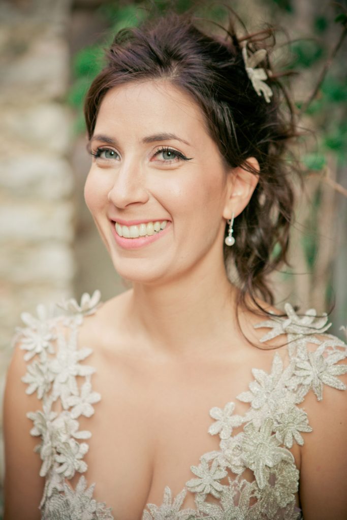 Romantic bride and groom portrait framed by soft greenery, captured against a rustic stone wall in a sun-washed Mediterranean setting. Their warm smiles and tender gaze create an intimate, timeless moment—perfect for destination wedding photography in a charming historic village.