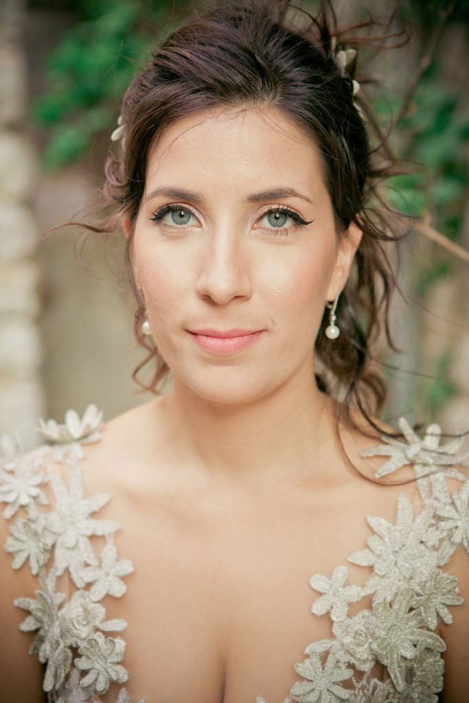 Romantic bride and groom portrait framed by soft greenery, captured against a rustic stone wall in a sun-washed Mediterranean setting. Their warm smiles and tender gaze create an intimate, timeless moment—perfect for destination wedding photography in a charming historic village.