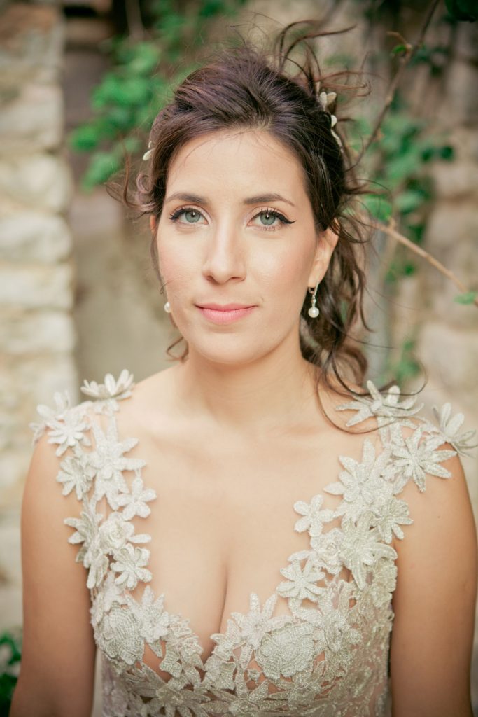 Romantic bride and groom portrait framed by soft greenery, captured against a rustic stone wall in a sun-washed Mediterranean setting. Their warm smiles and tender gaze create an intimate, timeless moment—perfect for destination wedding photography in a charming historic village.