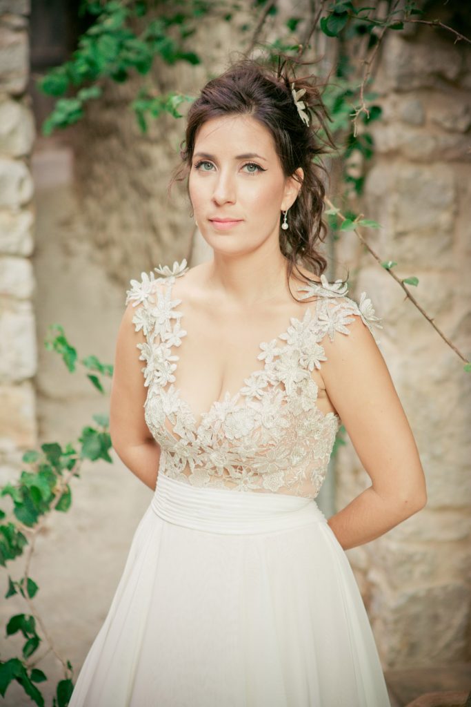 Romantic bride and groom portrait framed by soft greenery, captured against a rustic stone wall in a sun-washed Mediterranean setting. Their warm smiles and tender gaze create an intimate, timeless moment—perfect for destination wedding photography in a charming historic village.
