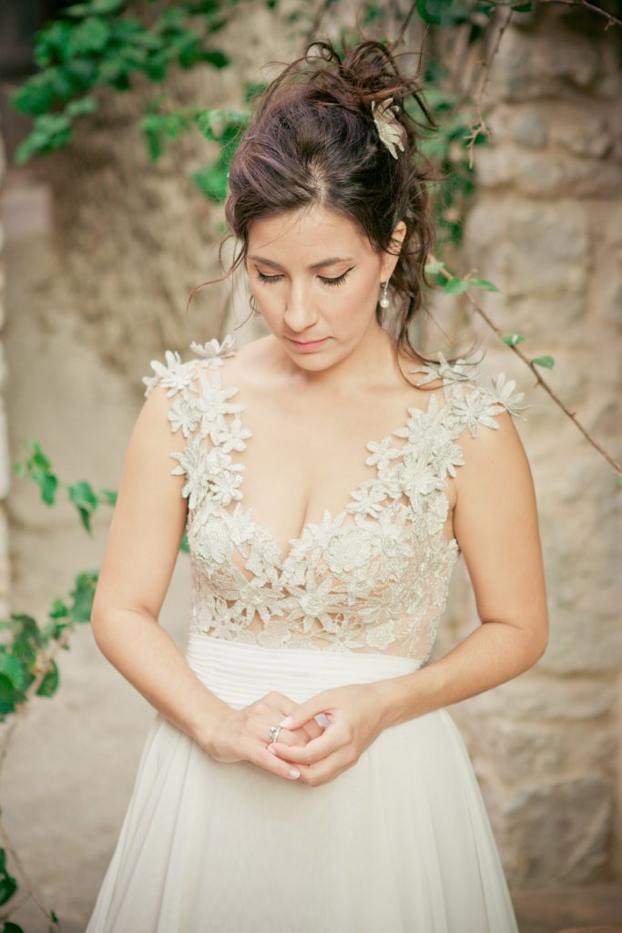 Romantic bride and groom portrait framed by soft greenery, captured against a rustic stone wall in a sun-washed Mediterranean setting. Their warm smiles and tender gaze create an intimate, timeless moment—perfect for destination wedding photography in a charming historic village.