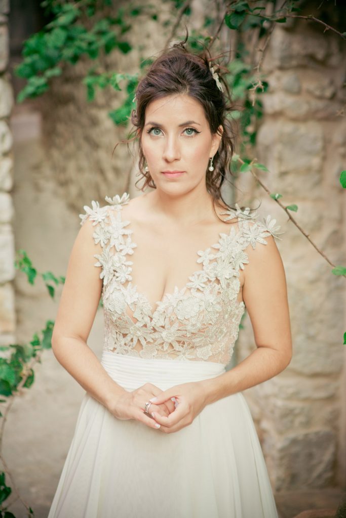 Romantic bride and groom portrait framed by soft greenery, captured against a rustic stone wall in a sun-washed Mediterranean setting. Their warm smiles and tender gaze create an intimate, timeless moment—perfect for destination wedding photography in a charming historic village.