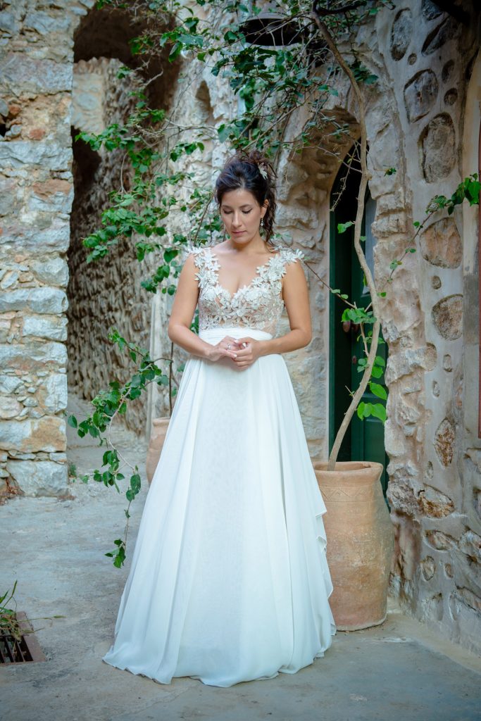 Romantic bride portrait framed by soft greenery, captured against a rustic stone wall in a sun-washed Mediterranean setting. Their warm smiles and tender gaze create an intimate, timeless moment—perfect for destination wedding photography in a charming historic village.