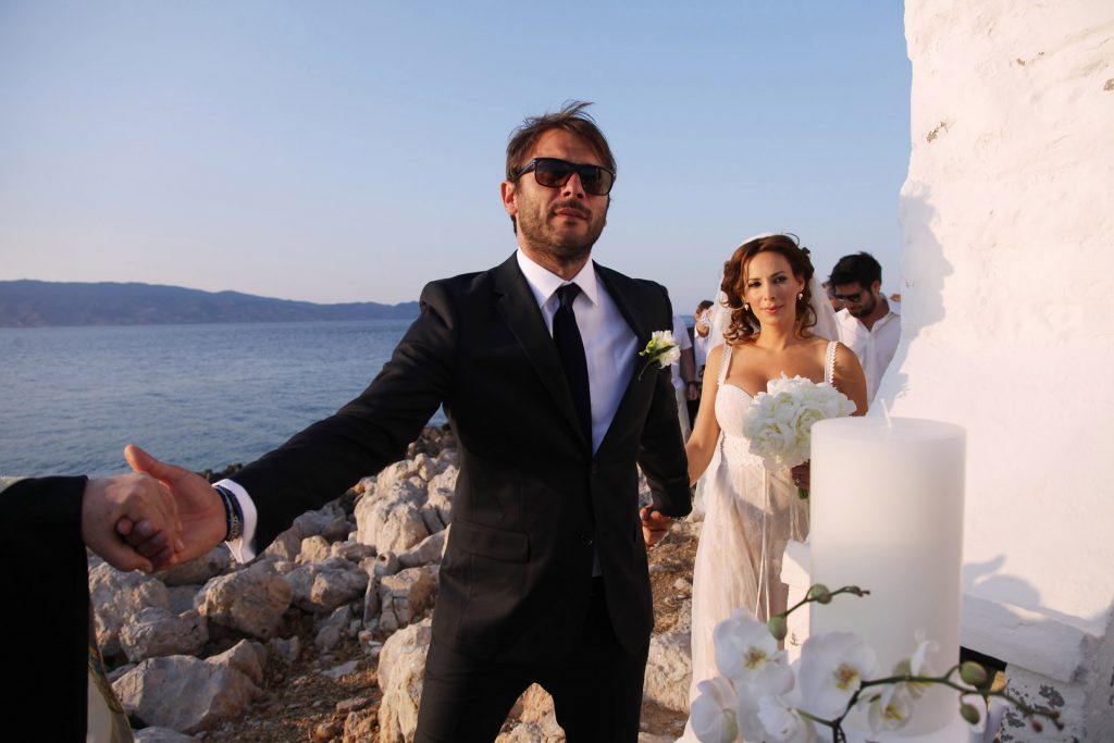 Groom leading bride white chapel Agios Nikolaos Hydra island Greece coastal wedding ceremony destination wedding photography