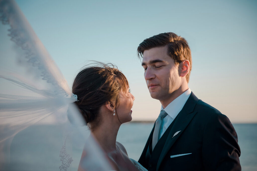 Bride and groom intimate portrait veil blowing wind coastal sunset Greece destination wedding photography