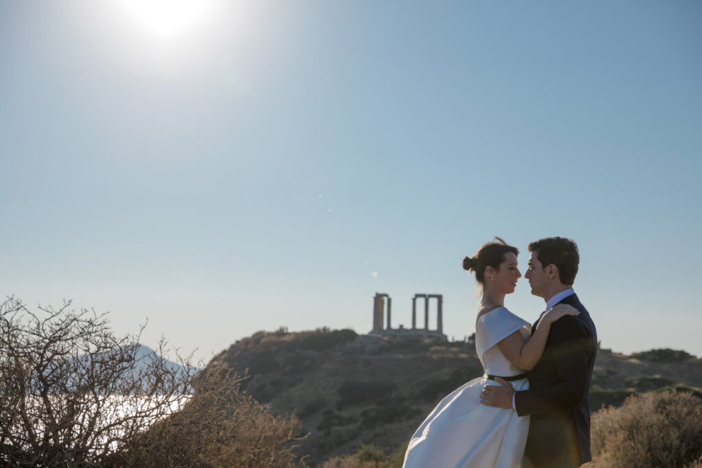 Bride and groom dramatic hilltop portrait dress flowing Cape Sounion Attica Greece coastal landscape destination wedding photography