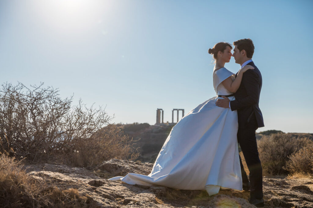 Bride and groom dramatic hilltop portrait dress flowing Cape Sounion Attica Greece coastal landscape destination wedding photography