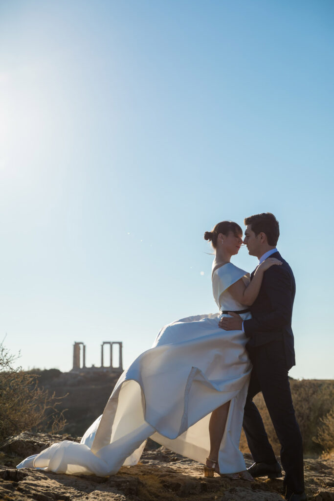 Bride and groom dramatic hilltop portrait dress flowing Cape Sounion Attica Greece coastal landscape destination wedding photography