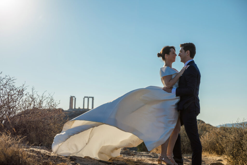 Bride and groom dramatic hilltop portrait dress flowing Cape Sounion Attica Greece coastal landscape destination wedding photography