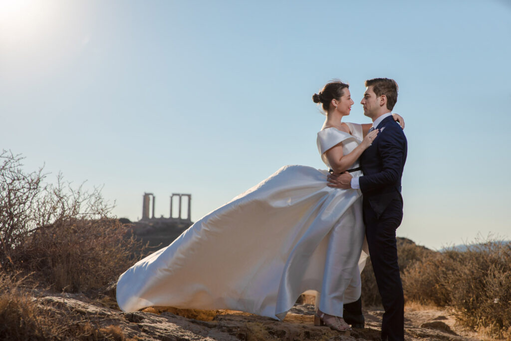 Bride and groom dramatic hilltop portrait dress flowing Cape Sounion Attica Greece coastal landscape destination wedding photography