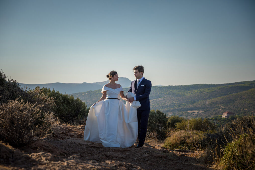 Bride and groom dramatic hilltop portrait dress flowing Cape Sounion Attica Greece coastal landscape destination wedding photography