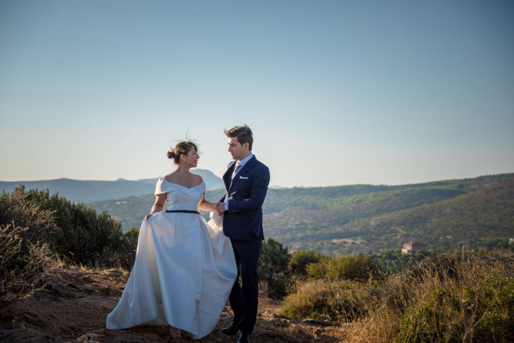 Bride and groom dramatic hilltop portrait dress flowing Cape Sounion Attica Greece coastal landscape destination wedding photography