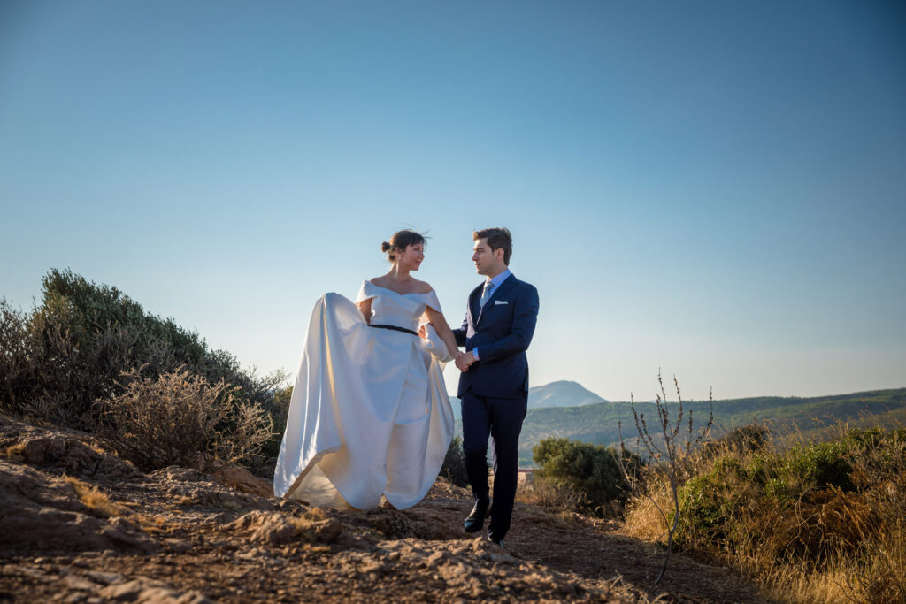 Bride and groom dramatic hilltop portrait dress flowing Cape Sounion Attica Greece coastal landscape destination wedding photography